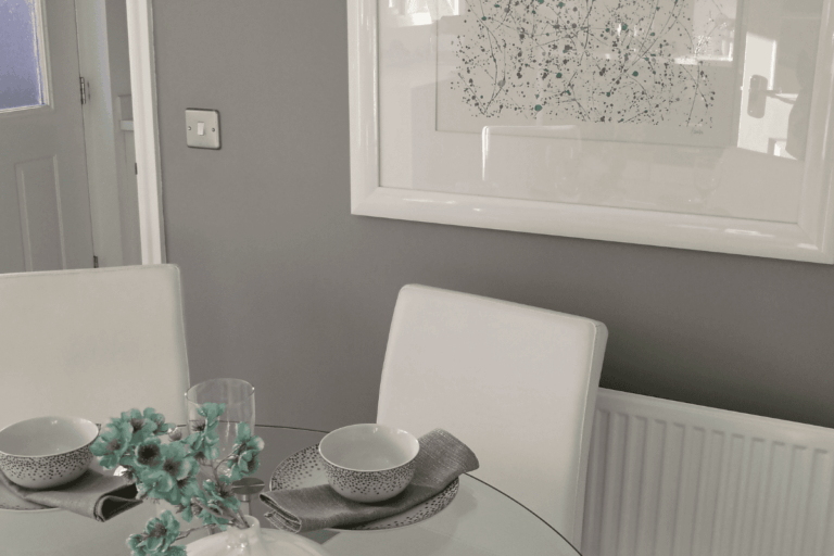 Feature image for a showhome visit blog post by Secret Home Designer. Images shows a dining room in a modern show home with light grey walls and white furnishings, glass dining table and white leather seating.