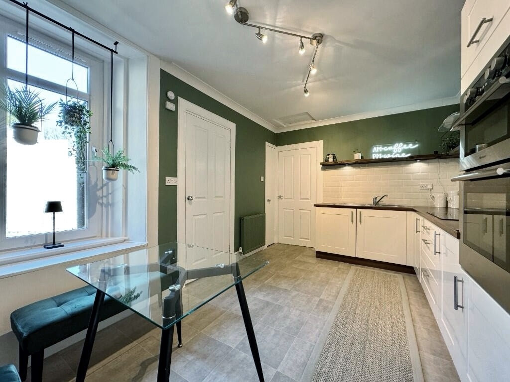 Modernised kitchen with dark green painted walls, open shelving, cream subway tile backsplash, open shelving and wood-effect countertop. After renovation image.
