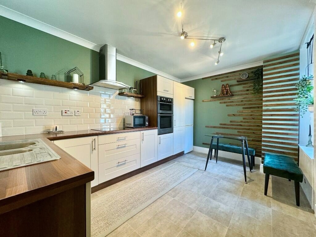 Modernised kitchen with dark green painted walls, open shelving, cream subway tile backsplash, open shelving and wood-effect countertop. After renovation image.