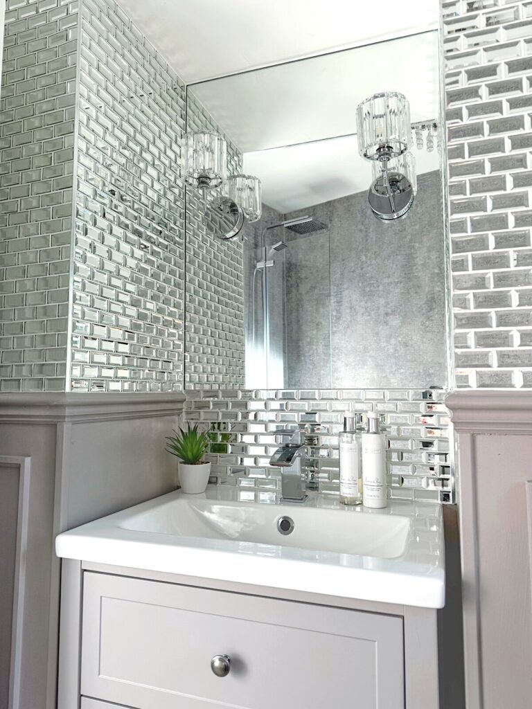 Stylish greige bathroom featuring rainfall shower and textured wet wall, along with a full wall of mirrored tiles above the panelling. Modern vanity unit and patterned flooring. Bathroom renovation after image.