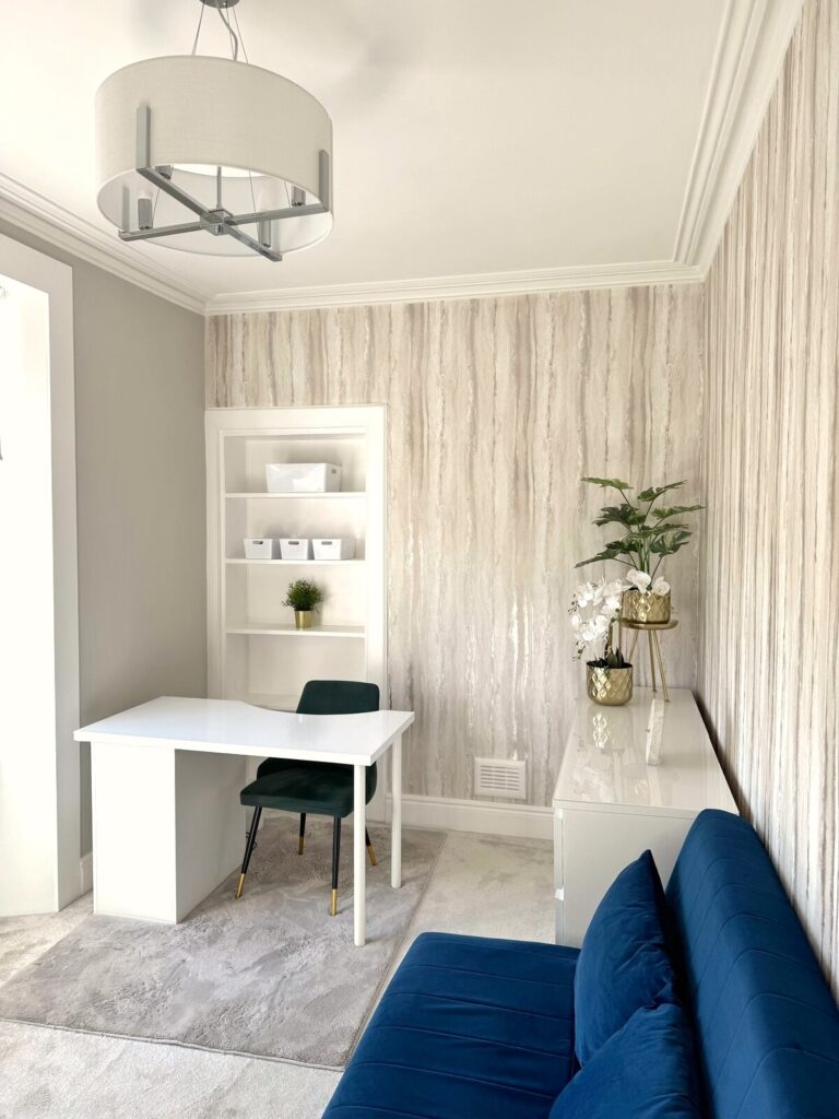 Stylish home office setup in spare room with white desk, shelves, and light metallic wallpaper. After renovation image.