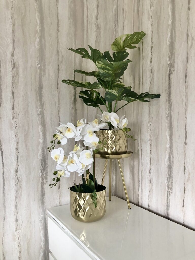 Faux Orchid Plant and Gold Planter Stands with Mixed Metallic Wallpaper in the Background
