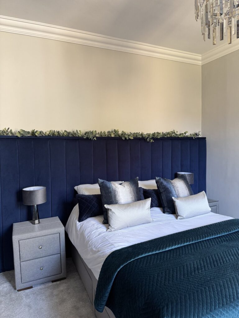 Luxury bedroom makeover with deep navy fluted velvet headboard, velvet bedding/throw and elegant crystal chandelier. Bedroom renovation after image.