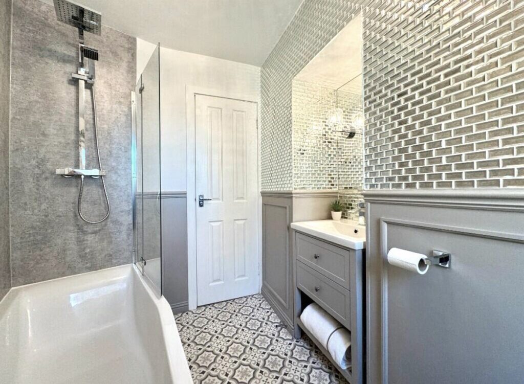 Stylish greige bathroom featuring rainfall shower and textured wet wall, along with a full wall of mirrored tiles above the panelling. Modern vanity unit and patterned flooring. Bathroom renovation after image.
