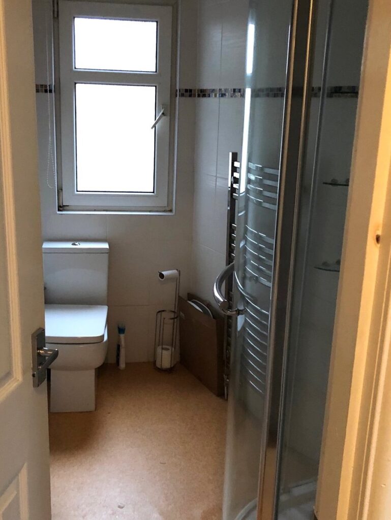 Photo of an outdated bathroom with orange vinyl and basic white fixtures. Before renovation image.