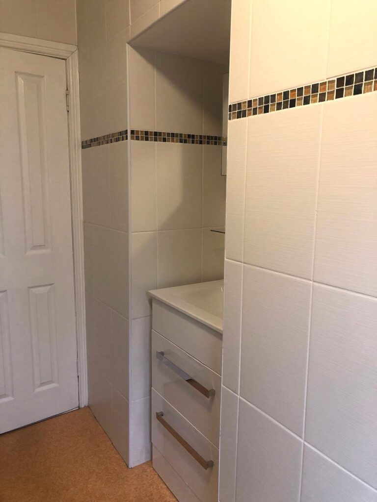 View of bathroom sink area with plain white tiled walls and dated orange vinyl. Before renovation image.