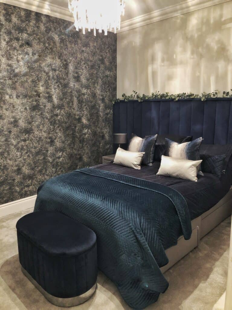 Luxury bedroom makeover with moody dark navy wallpaper, deep navy fluted velvet headboard, and elegant crystal chandelier. Bedroom renovation after image.