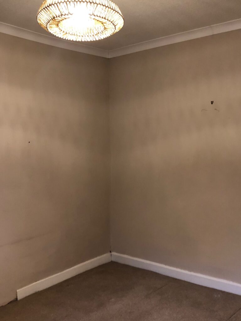 Bare bedroom corner before makeover, with beige walls, scuffed paint, and an exposed ceiling light. Before bedroom renvoation image.
