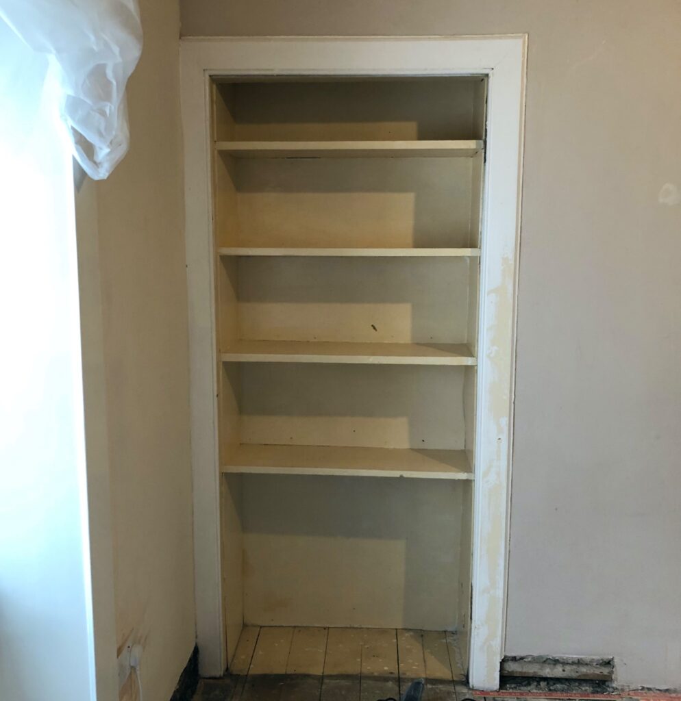 Unfinished built-in shelving area in a bedroom, bare wooden shelves and unpainted walls. Before bedroom renovation image.
