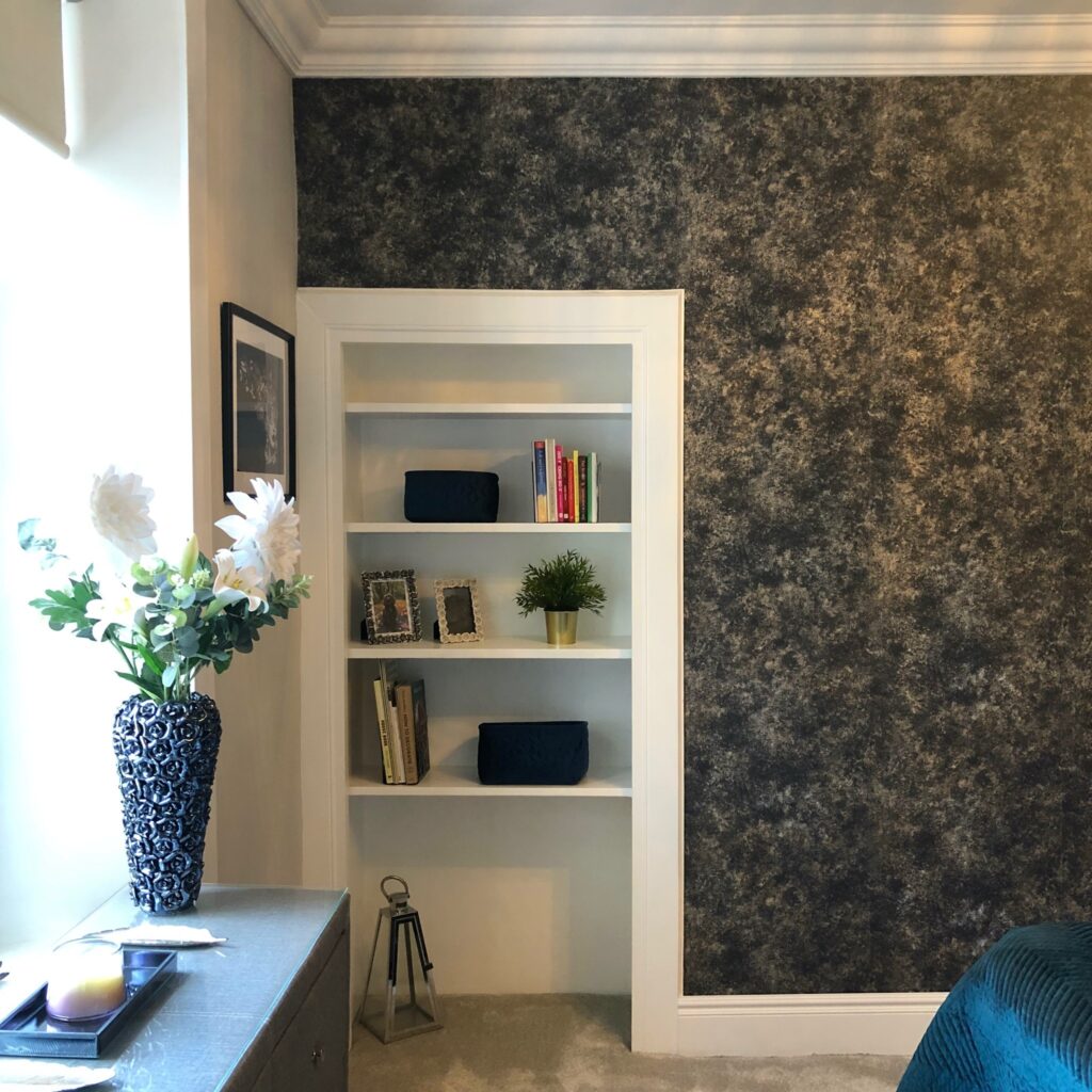 Modernised Victorian home built-in shelving area in a renovated bedroom with soft grey paint, decorative accessories on the shelves, and a dark navy textured feature wallpaper. After bedroom renovation image.