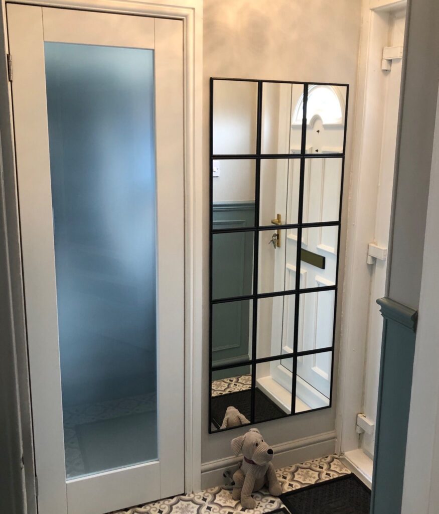 Brightly renovated entrance area with patterned flooring, frosted glass door, and decorative wall mirror with black detail. After renovation image.