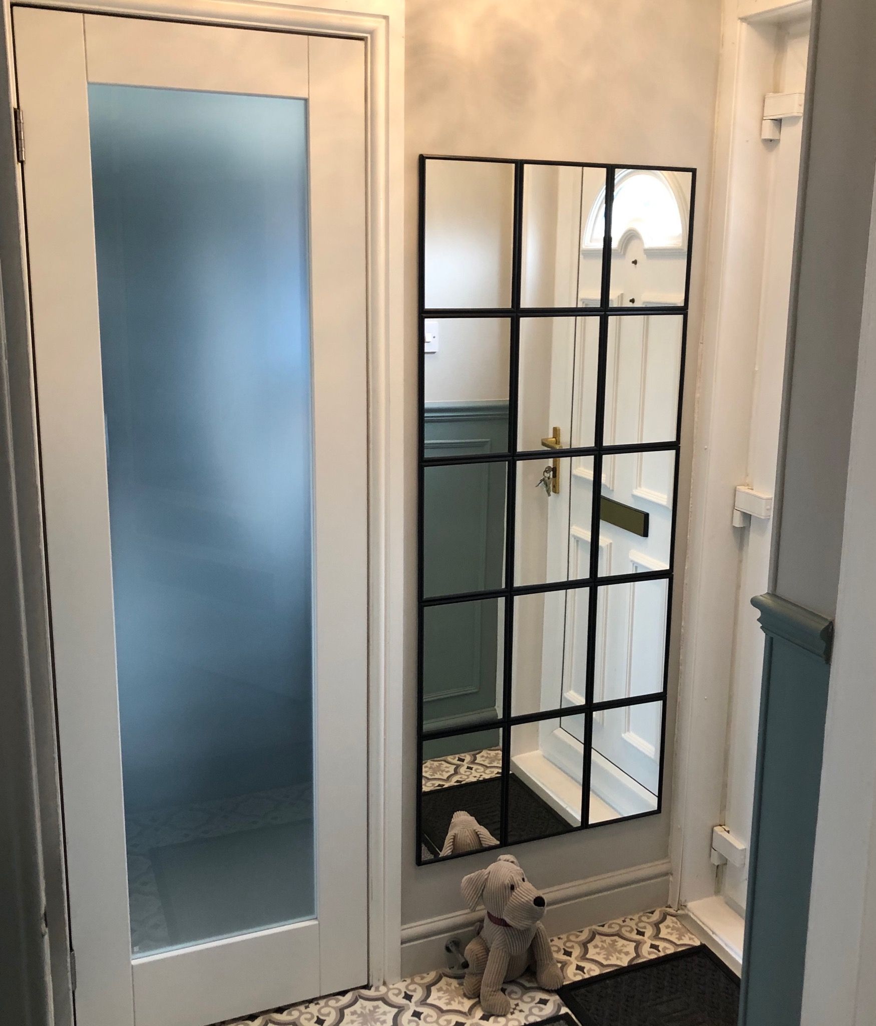 Brightly renovated entrance area with patterned flooring, frosted glass door, and decorative wall mirror with black detail. After renovation image.