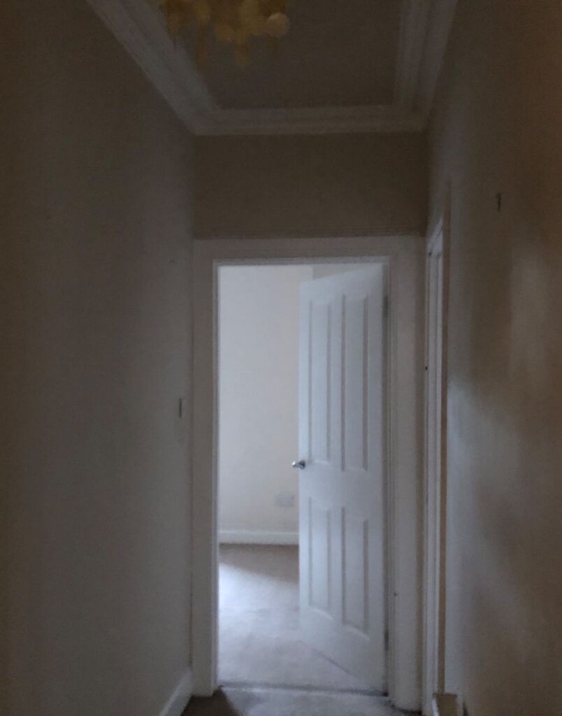 Dimly lit hallway before renovation with plain beige walls and minimal natural light. Before renovation image.