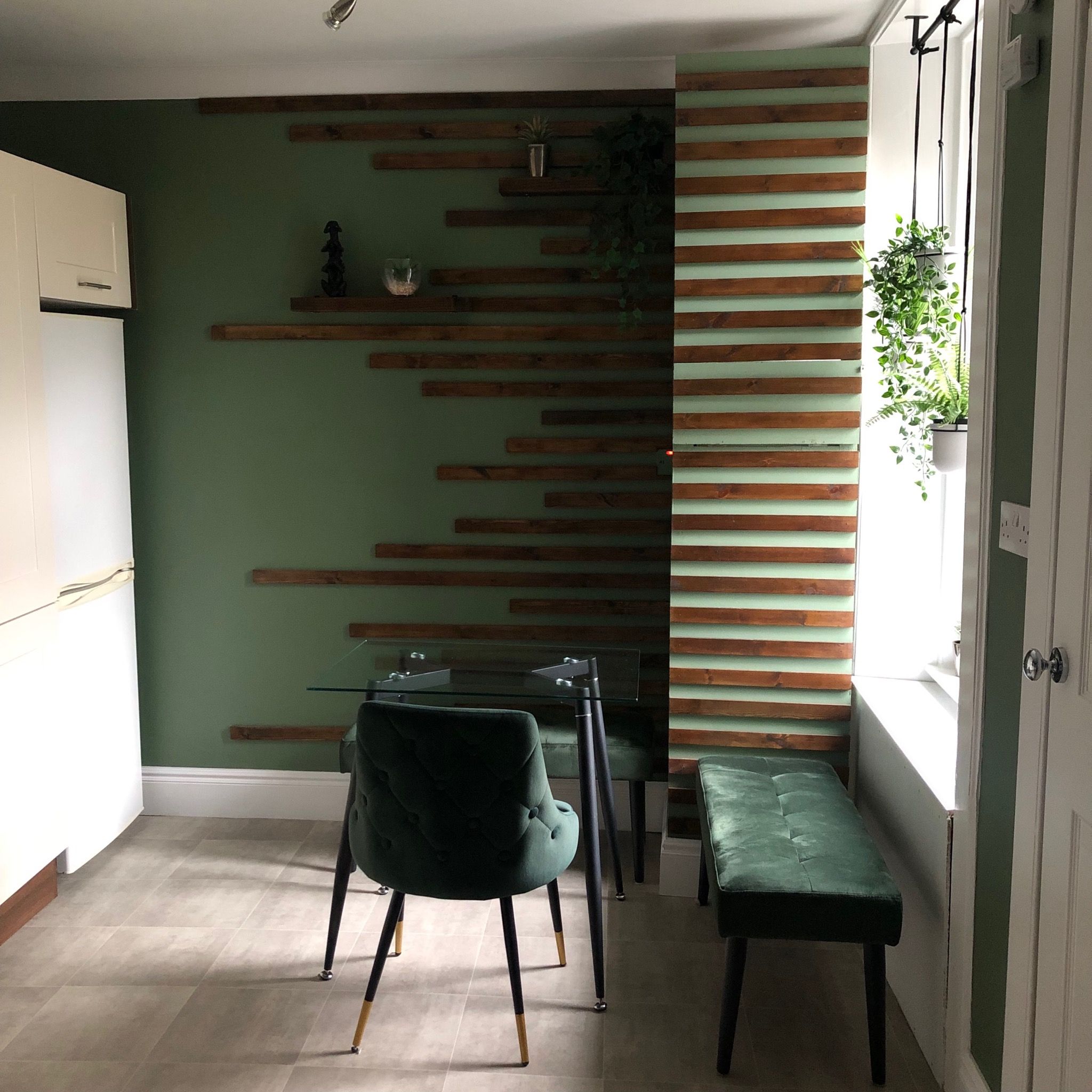 Renovated kitchen with modern dark green feature walls, wooden slat detail, and green velvet dining chairs. After renovation image.