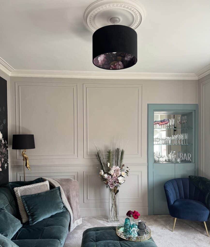 Stylish living room with statement black lampshade, velvet teal sofa, and decorative wall panelling. After renovation image.