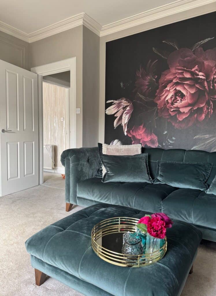 Living room renovation after image. View with teal green velvet sofa, floral mural wallpaper, and velvet teal ottoman with gold tray and accessories. After renovation image.