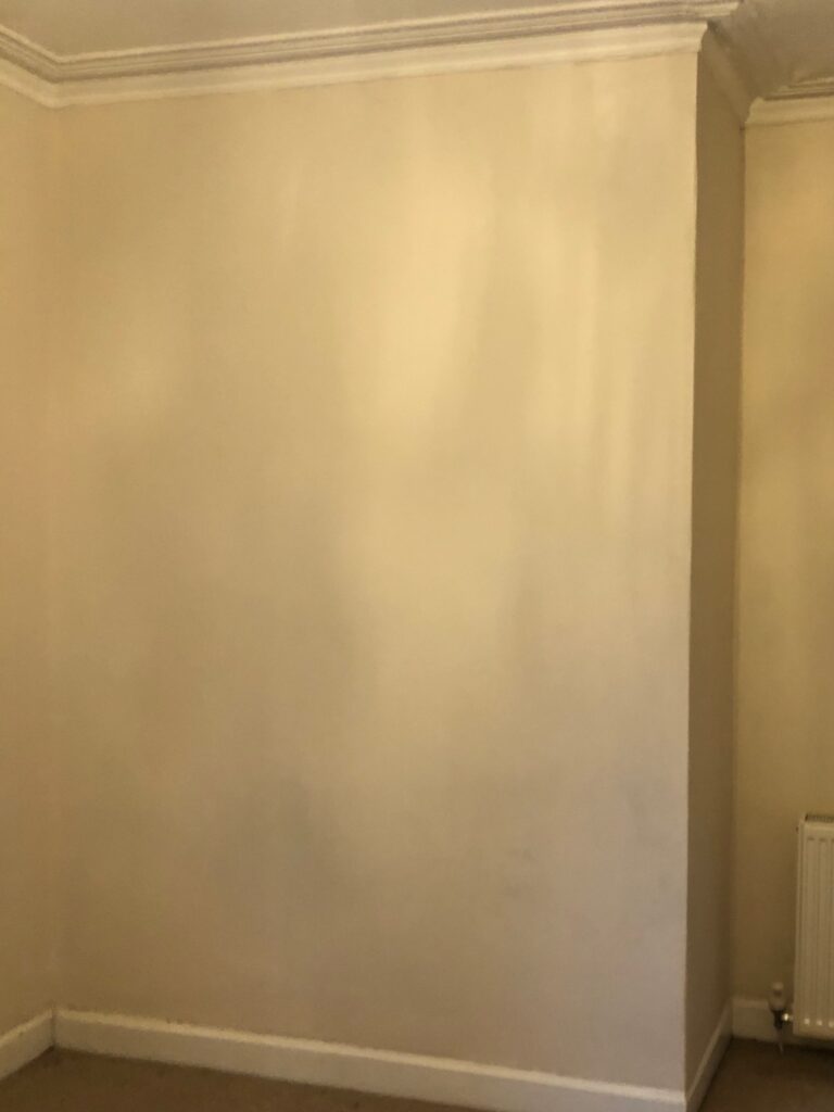 Before image of plain beige living room wall with radiator. Before renovation image.