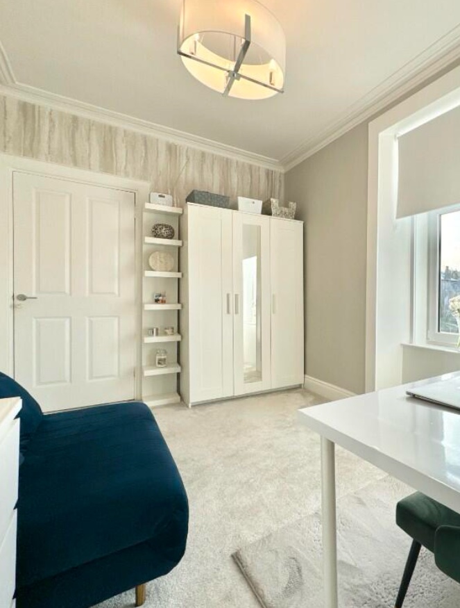 Bright and airy guest/office room featuring white wardrobe, shelving, and light metallic wallpaper. After renovation image.