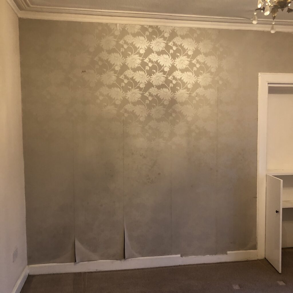Dated bedroom before renovation - peeling wallpaper and pinky beige paint.