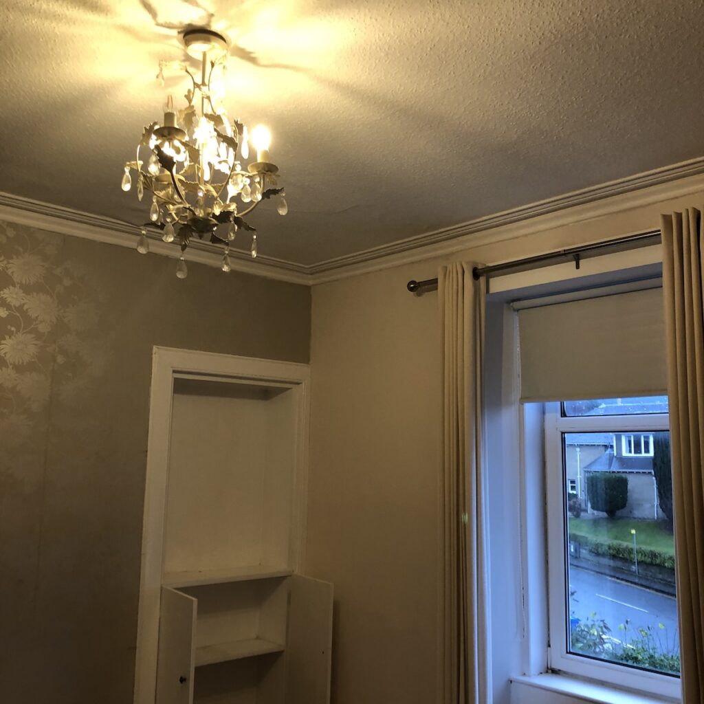 Dated bedroom before renovation - peeling wallpaper and pinky beige paint.