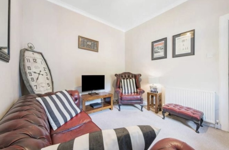 Estate Agents image from the time of sale. Older style of living room with brown leather chesterfield.