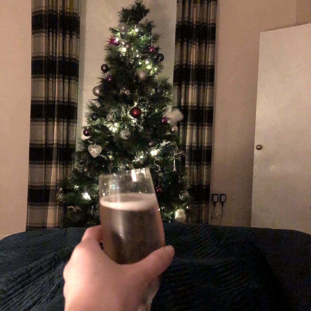 Move in day - Glass of bubbles to celebrate, in the background - christmas tree and stripe curtains.