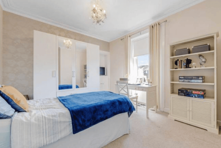 Date bedroom before renovation - bed, wardrobe, long curtains, shelving unit - all pinky-beige colour.