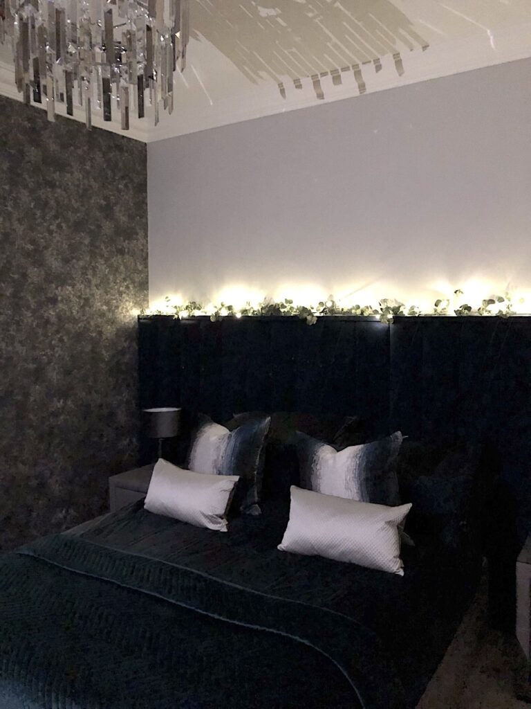 Main bedroom renovation complete. Dark moody vibe - image showing dark textured wallpaper, high headboard and velvet bedding and cushions.
