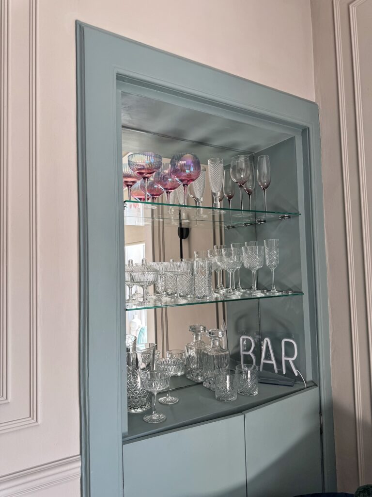 Bar area in living room, with mirror background and glass shelves with glassware displayed