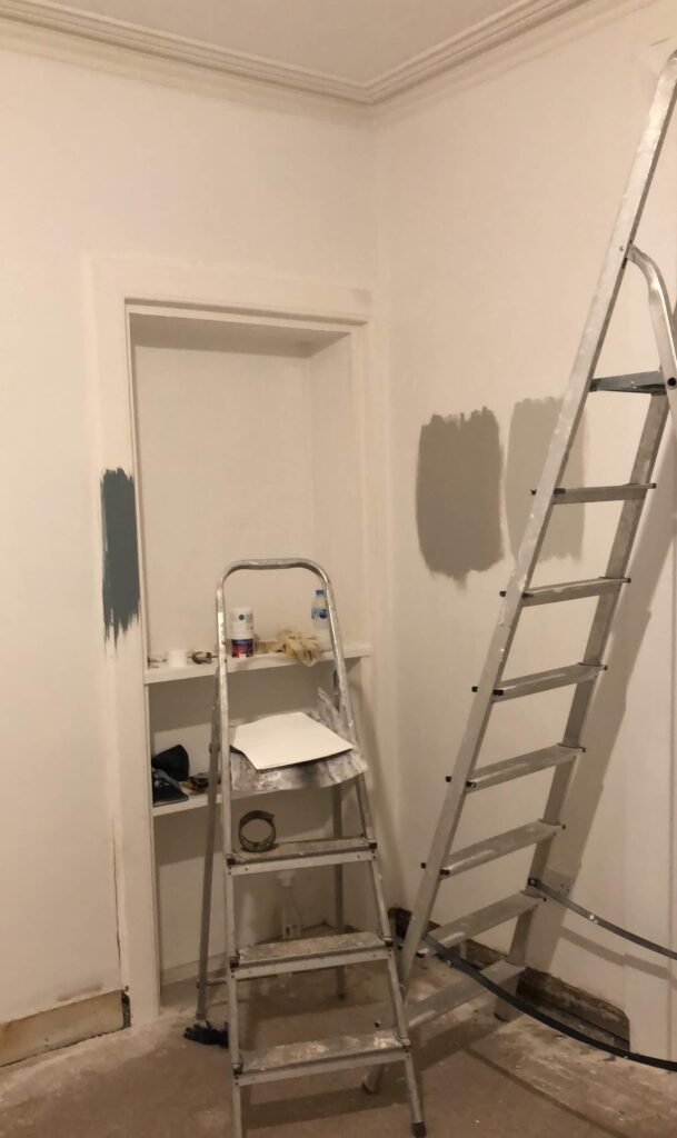 Living Room Mid Renovation, showing different paint samples on wall and ladders in foreground